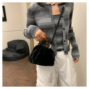 Détail d'un sac seau en fausse fourrure noire avec poignée perlée ambre sur un modèle