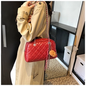Detail of red quilted chain crossbody bag with a plush bear charm on trench coat