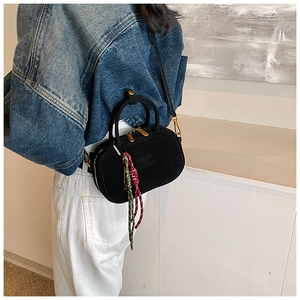 Détail du sac à main noir en daim mat avec finitions dorées et breloque tressée