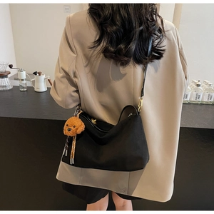 Detail view of black crescent shoulder bag with golden clasp and brown teddy dog pendant