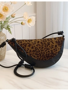 Leopard print and black leather crescent bag with knot detail on white marble surface