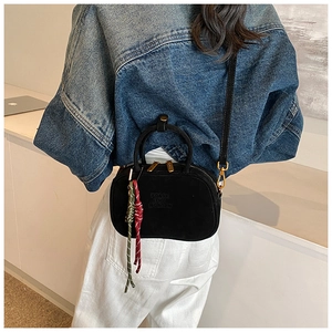 Détail d'un sac bandoulière en daim noir avec lettrage embossé et breloques tressées