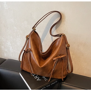 Detailed close-up of brown faux leather tote bag with side zippers and bow decoration