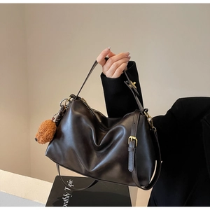Macro shot of dark brown leather handbag featuring brass hardware and a plush bear charm