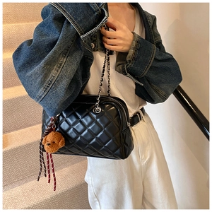 Close-up of quilted black crossbody bag featuring a silver chain and teddy bear charm