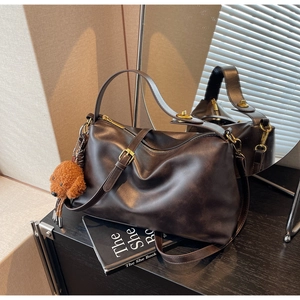 Detail of dark brown leather tote with gold hardware and plush poodle charm accessory