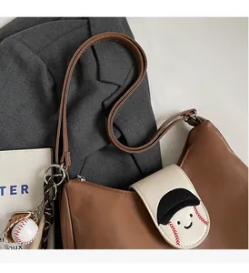 Detail of a brown and beige shoulder bag with baseball embroidery and a themed charm