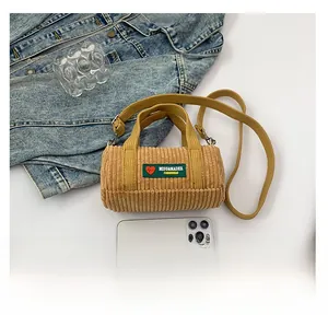 Dettaglio borsa cilindrica in velluto a coste marrone con patch logo e trama fine