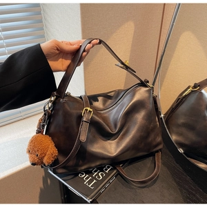 Close-up of retro brown leather tote with adjustable strap and plush puppy charm
