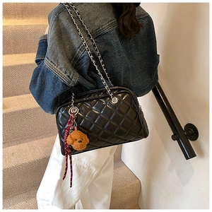 Detail of black quilted leather shoulder bag with chain strap and teddy bear charm