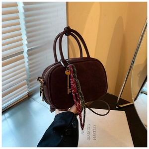 Détail du sac bowling en daim marron avec breloque clé dorée et tirette de zip tissée