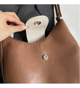 Macro view of brown leather half-moon bag featuring round magnetic metal closure and cream interior