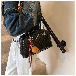 Detail of black quilted shoulder bag with silver chain and cute plush bear charm