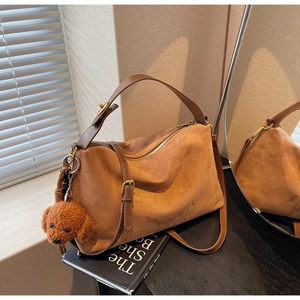 Macro detail of brown suede tote bag featuring a cute plush teddy dog charm and metallic zipper