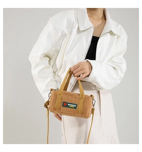 Detailed texture of brown corduroy cylinder bag with logo tag and woven straps