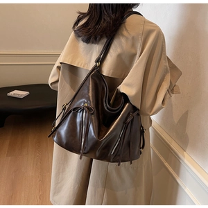 Deep brown retro hobo bag with tassel detail worn by model in beige trench coat