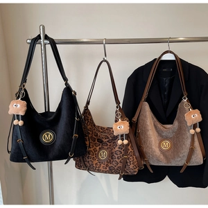 Three corduroy leopard tote bags with M metal logos and plush charms on a rack