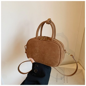 Détail d'un sac bowling en daim marron avec gaufrage de la marque et zip métallique