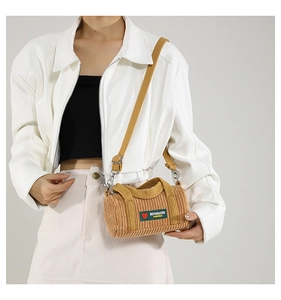 Detail of khaki corduroy cylinder bag featuring green label and yellow shoulder strap