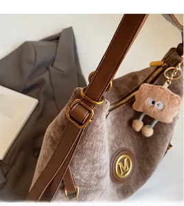 Detail of velvet brown tote with leather strap, gold M logo and plush cookie charm