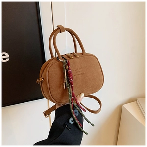 Détail du sac à main en daim caramel avec logo embossé et breloques à pompons tissés