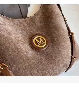 Detail of taupe velvet tote bag featuring a gold M logo and brown leather strap
