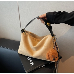 Detail of khaki suede tote bag with black leather handle and plush teddy bear charm