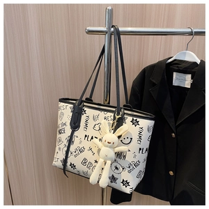 Graffiti tote bag detail with plush bunny charm hanging on a modern metal rack