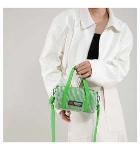 Detail of green corduroy cylindrical bag with metal D-ring and brand label tag
