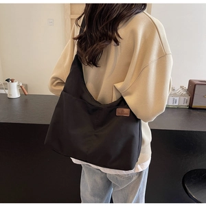 Détail d'un grand sac cabas en toile noir avec étiquette en cuir sur un mannequin femme