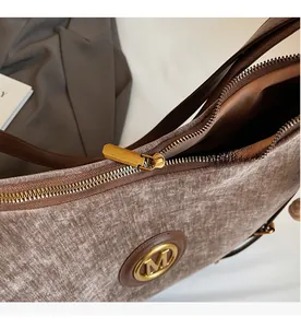 Detail of smooth gold metal zipper and 'M' logo on brown velvet shoulder bag