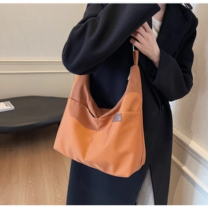 Gros plan du sac fourre-tout orange en toile avec poche latérale et logo porté par le modèle