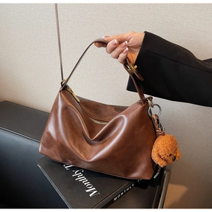 Detailed shot of a brown leather tote bag with a plush dog charm on textured background