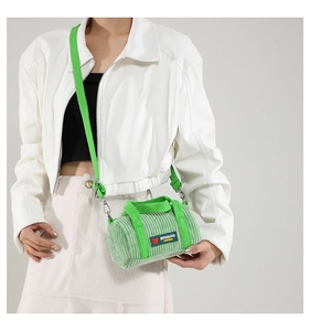 Detail of green corduroy cylindrical bag with woven straps on white jacket outfit