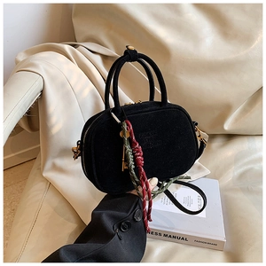 Détail du mini sac Boston en daim noir avec gland tissé et clé dorée sur fond de cuir