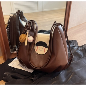 Detail of a brown leather hobo bag featuring a baseball smiley face and themed charms