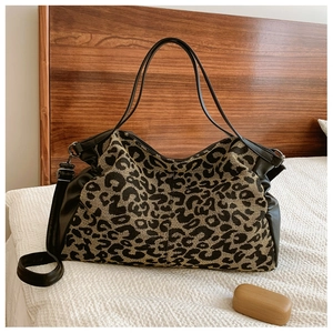 Detailed view of leopard print tote bag with black leather straps on a white textured bed