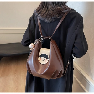 Detail of dark brown pleated backpack with white cartoon flap and baseball charm charm