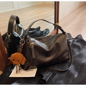 Detail of dark brown leather tote featuring gold zippers and a plush puppy charm