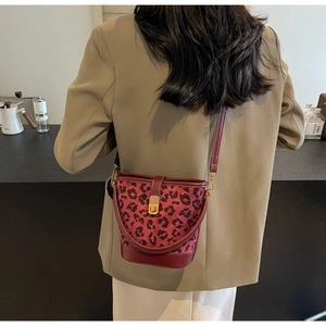 Mini borsa a secchiello leopardata con bordo rosso e chiusura dorata su blazer beige
