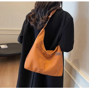 Détail d'un grand sac hobo en toile marron avec large bandoulière et écusson de mode