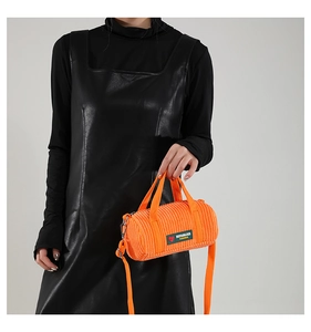 Detail of orange corduroy barrel bag featuring heart label and detachable shoulder strap