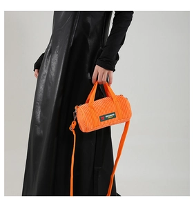 Detail of orange corduroy barrel bag with logo label and detachable fabric shoulder strap