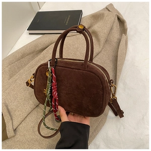 Détail du sac à main en daim marron foncé avec fermeture éclair dorée et breloque tressée