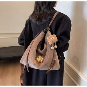 Brown retro tote bag with metal M logo and plush charm shown on person for scale
