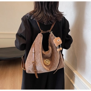 Detail of brown plush backpack with a metal M logo and adjustable leather straps