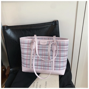Detail of pink plaid tote bag featuring leather handles and brand logo tag on black chair