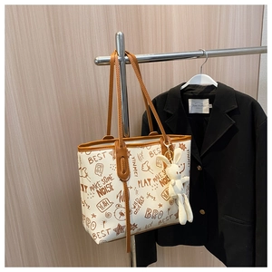 Close-up of white tote bag featuring artistic graffiti prints and a plush rabbit pendant