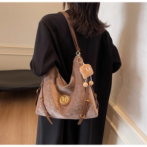 Detail of tan suede tote bag with leather straps and a plush toast charm on shoulder
