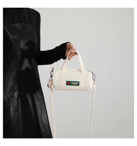 Dettaglio della borsa a cilindro in velluto bianco con etichetta verde e fibbie argentate